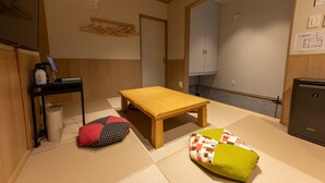 A room with tatami flooring, a wooden table, a small black trash bin, and a refrigerator. - Irodori Hotel MOMO (fukuokashi,hakataku,katakasu)