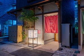 A traditional Japanese building with a red banner, a signboard, and a small tree. - Irodori Hotel MOMO (fukuokashi,hakataku,katakasu)