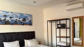A hotel room with a large bed, a painting of a mountain landscape, a black metal shelf unit, and a mirror with a green curtain. - Les Villas du Douar (Marrakech)