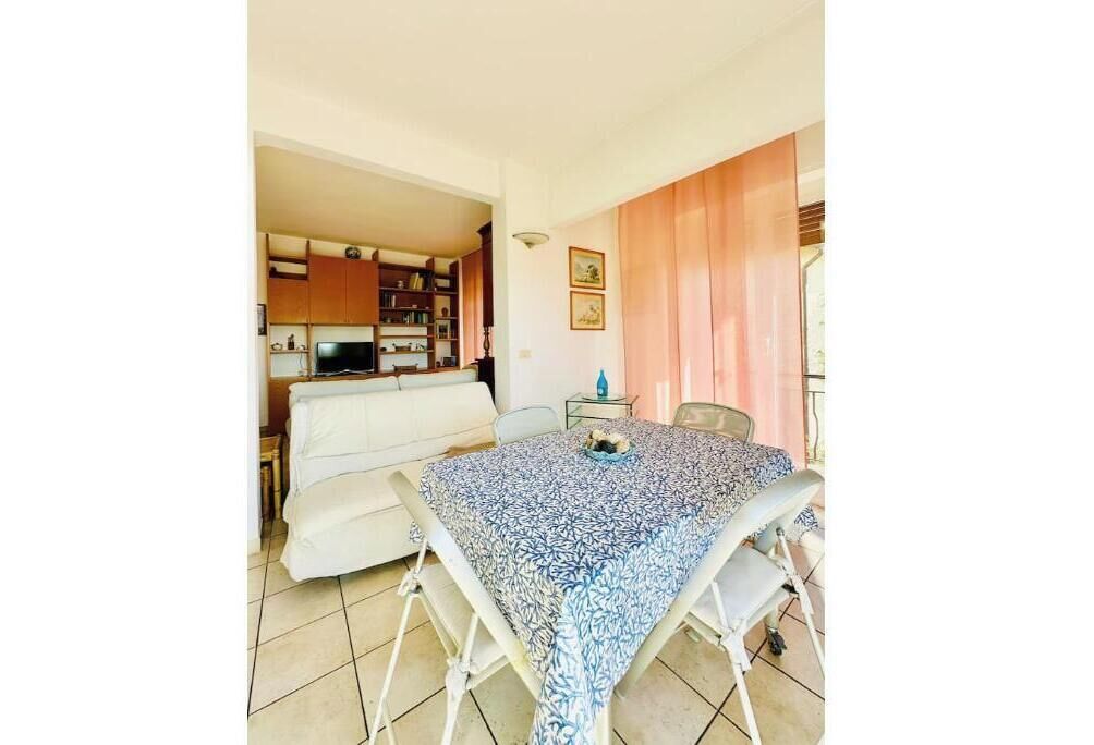 A dining area with a table and chairs, a sofa, and a kitchen in the background.