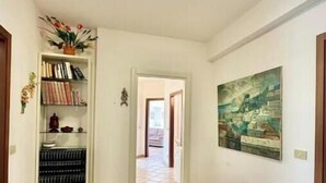 Ein Korridor mit Fliesenboden, einem Bücherregal voller Bücher, einem Gemälde an der Wand und einer Bank.