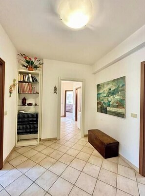 Un corridoio con pavimento piastrellato, una libreria piena di libri, un quadro appeso al muro e una panca.