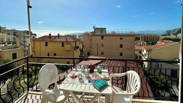 Ein Balkon mit Tisch und Stühlen, mit Blick auf eine Stadtlandschaft aus Gebäuden unter blauem Himmel.