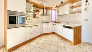 Eine moderne Küche mit weißen Schränken, einem eingebauten Backofen, einem Herd und Holzregalen.