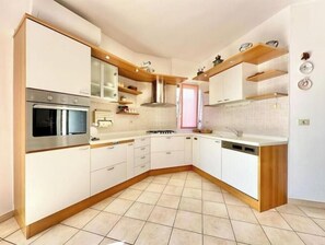 Una cucina moderna con mobili bianchi, forno integrato, piano cottura ed mensole in legno.