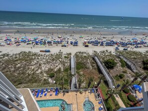 Ein Strand mit vielen Sonnenschirmen und Liegestühlen, ein Poolbereich mit Liegen und Blick auf den Ozean.