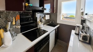 A modern kitchen with a black stove, white countertops, and a window overlooking a scenic view. - Duplex sea view, pets welcome, parking - 6 guests (Merville-Franceville-Plage)