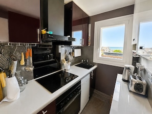 A modern kitchen with a black stove, white countertops, and a window overlooking a scenic view. - Duplex sea view, pets welcome, parking - 6 guests (Merville-Franceville-Plage)