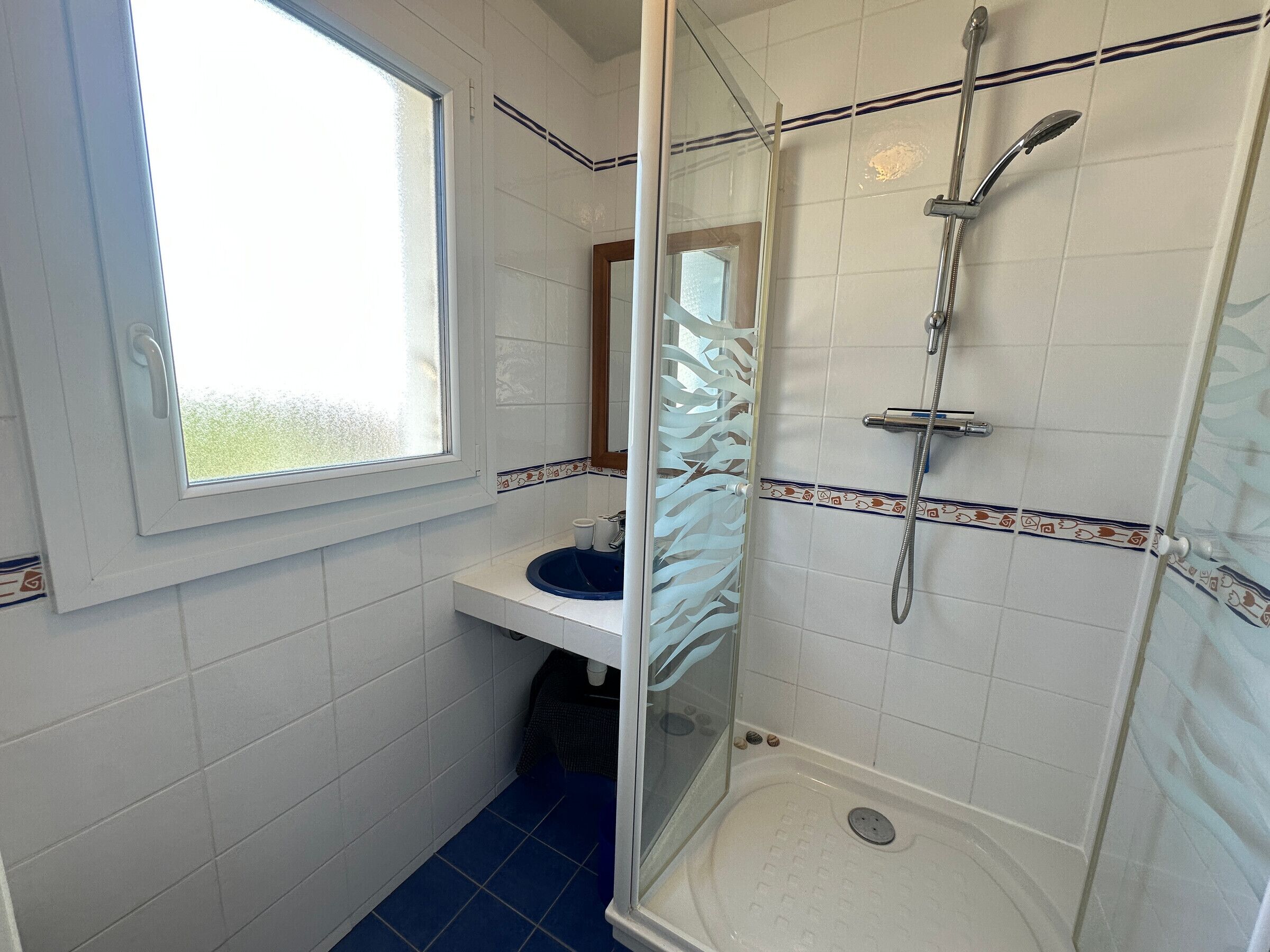 Un baño con ducha, lavamanos, ventana y espejo.