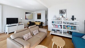 Ein Wohnzimmer mit Sofa, Couchtisch, Bücherregal, Fernseher und Essbereich.