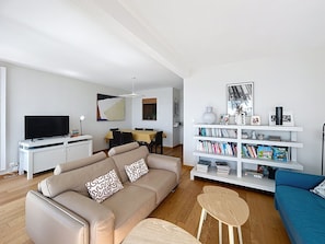Un salon comprenant un canapé, une table basse, une bibliothèque, un téléviseur et un coin repas.