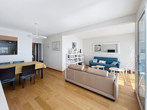 Un salon moderne comprenant un canapé, une table à manger, des chaises, une bibliothèque et une grande fenêtre.