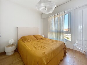 Une chambre à coucher comprenant un lit, une table de chevet, une chaise, une fenêtre avec des rideaux et un luminaire au plafond.