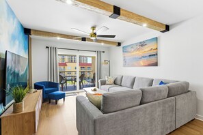 Ein modernes Wohnzimmer mit einem grauen Sofa, einem blauen Sessel, einem Holztisch und einem Deckenventilator.
