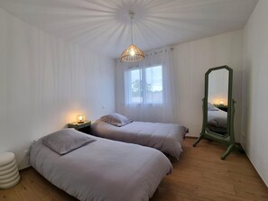 Ein Schlafzimmer mit zwei Betten, einem Fenster, einem Spiegel und einer Pendelleuchte.