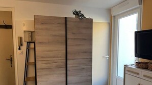 Una habitación con un armario de madera grande, una escalera, un televisor sobre un mueble y una puerta que da a otra estancia.