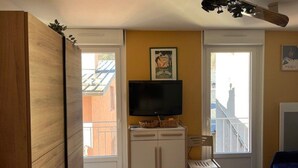 Habitación pequeña con una televisión sobre un mueble, una silla, una mesita con cuencos y una cama.