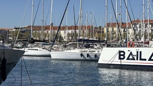 Un puerto deportivo con varios veleros amarrados, edificios al fondo y un cielo despejado.