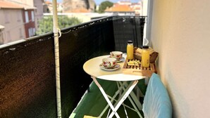 Un balcón con una pequeña mesa, una silla, una botella de jugo y una cesta de pan.