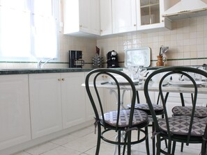 A kitchen with white cabinets, a coffee machine, and a glass-top table with chairs. - Charming house - 4 guests, near beach (La Brée-les-Bains)