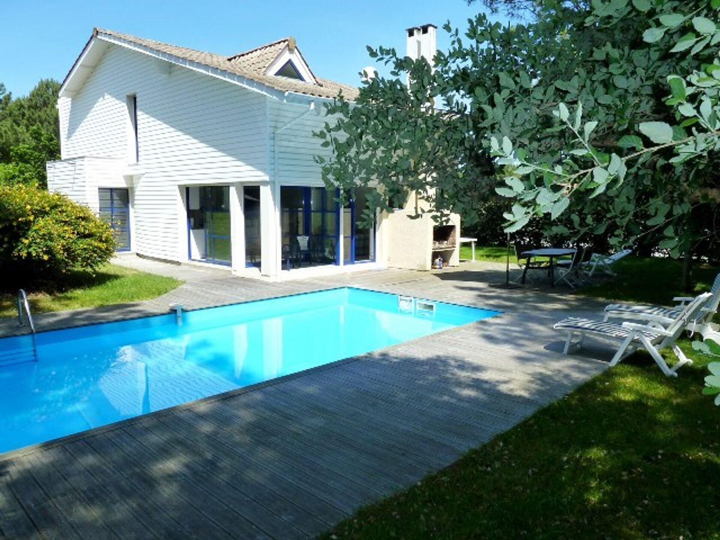 Ein Haus mit Schwimmbad, Terrasse und Baum.