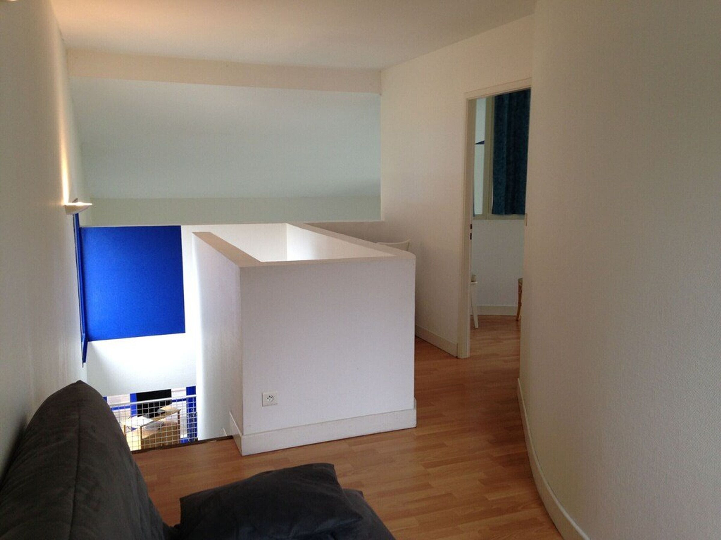 Una stanza con un letto bianco, un separé blu e un pavimento in legno.