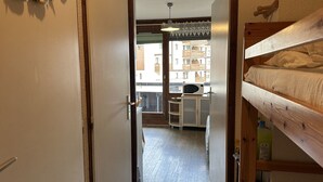 Un corridoio stretto che conduce a una stanza con un letto a castello, un forno a microonde su un tavolino e vista sugli edifici esterni.