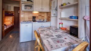 Angolo cottura compatto con frigorifero, forno a microonde e macchina del caffè. Un letto con copripiumino trapuntato e una panca in legno.