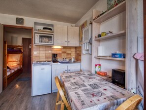 Eine kleine Küche mit Kühlschrank, Mikrowelle und Kaffeemaschine. Ein Bett mit gesteppter Auflage und eine hölzerne Sitzbank.