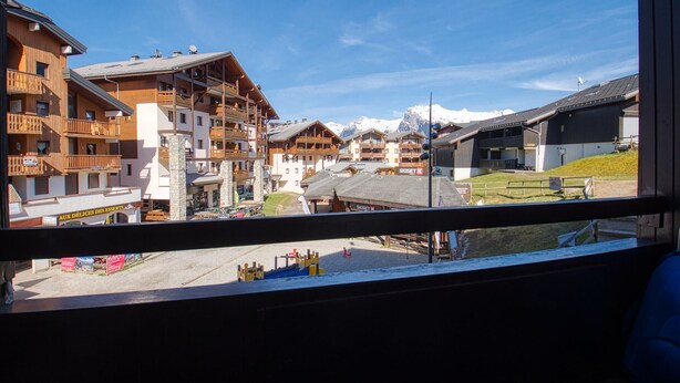 Vista di una località montana con edifici in legno, una seggiovia e montagne innevate sullo sfondo.