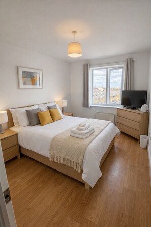 A bedroom with a bed, bedside tables, a TV, a window, and a city view. - Northfleet-luxury 2 bed apartment (Gravesend)