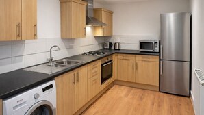 Una cocina moderna con armarios de madera, electrodomésticos de acero inoxidable, horno integrado y lavadora.