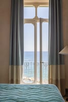 Una habitación con cama, cortinas y vistas al mar desde un balcón.