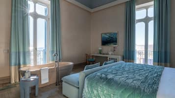 Habitación de hotel con una cama grande, una zona de estar con una silla, un escritorio y una bañera.