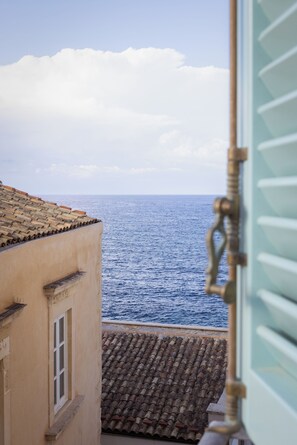 A coastal view from a window overlooking the sea, with a building's tiled roof and a glimpse of a door handle.
