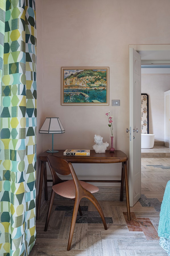 A room with a wooden desk, a chair, a framed painting, a vase with flowers, and a patterned curtain. - EGEO - Ortigia (Syracuse)