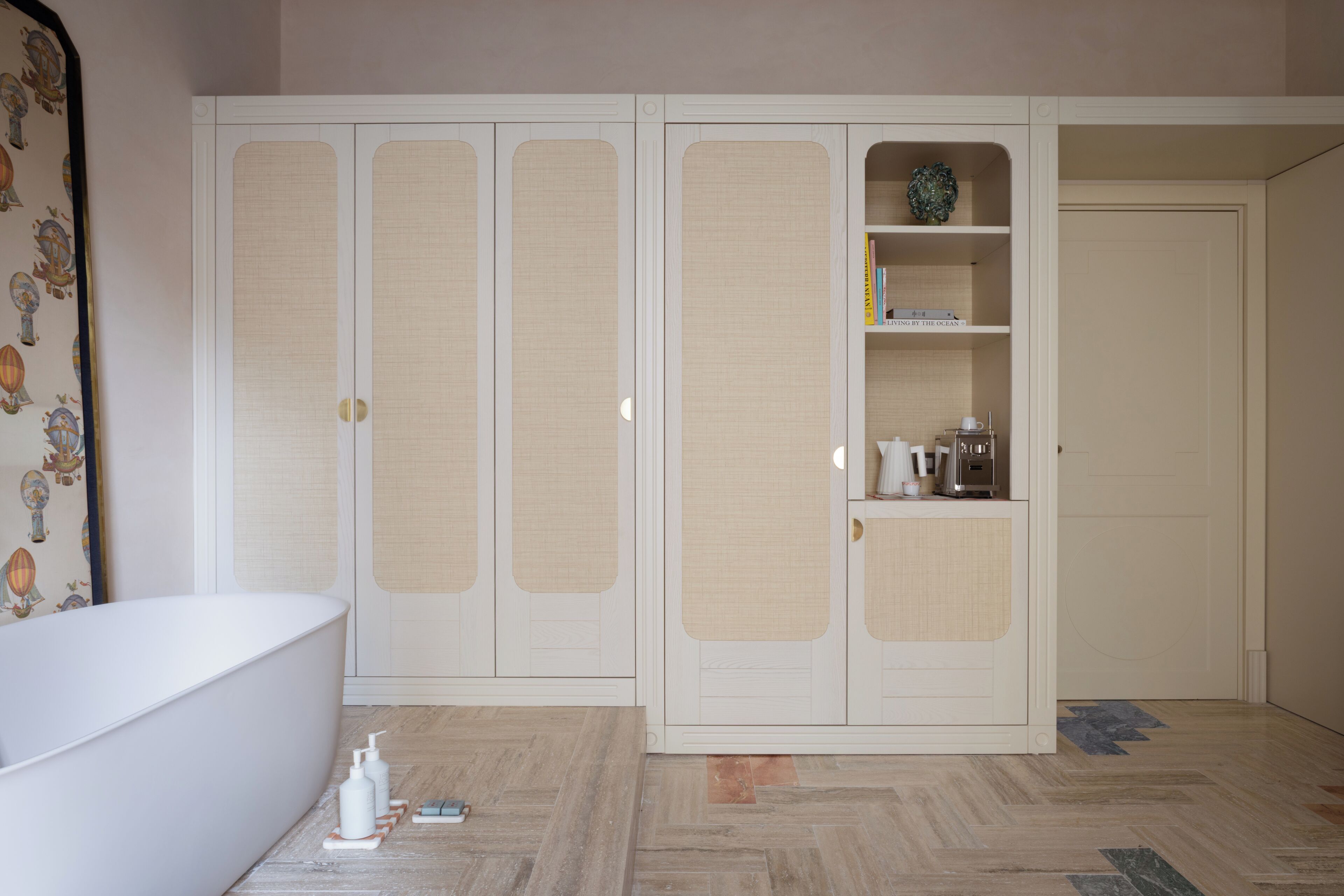 A bathroom with a white bathtub, a mirror with a decorative border, and a wardrobe with a mirrored door.