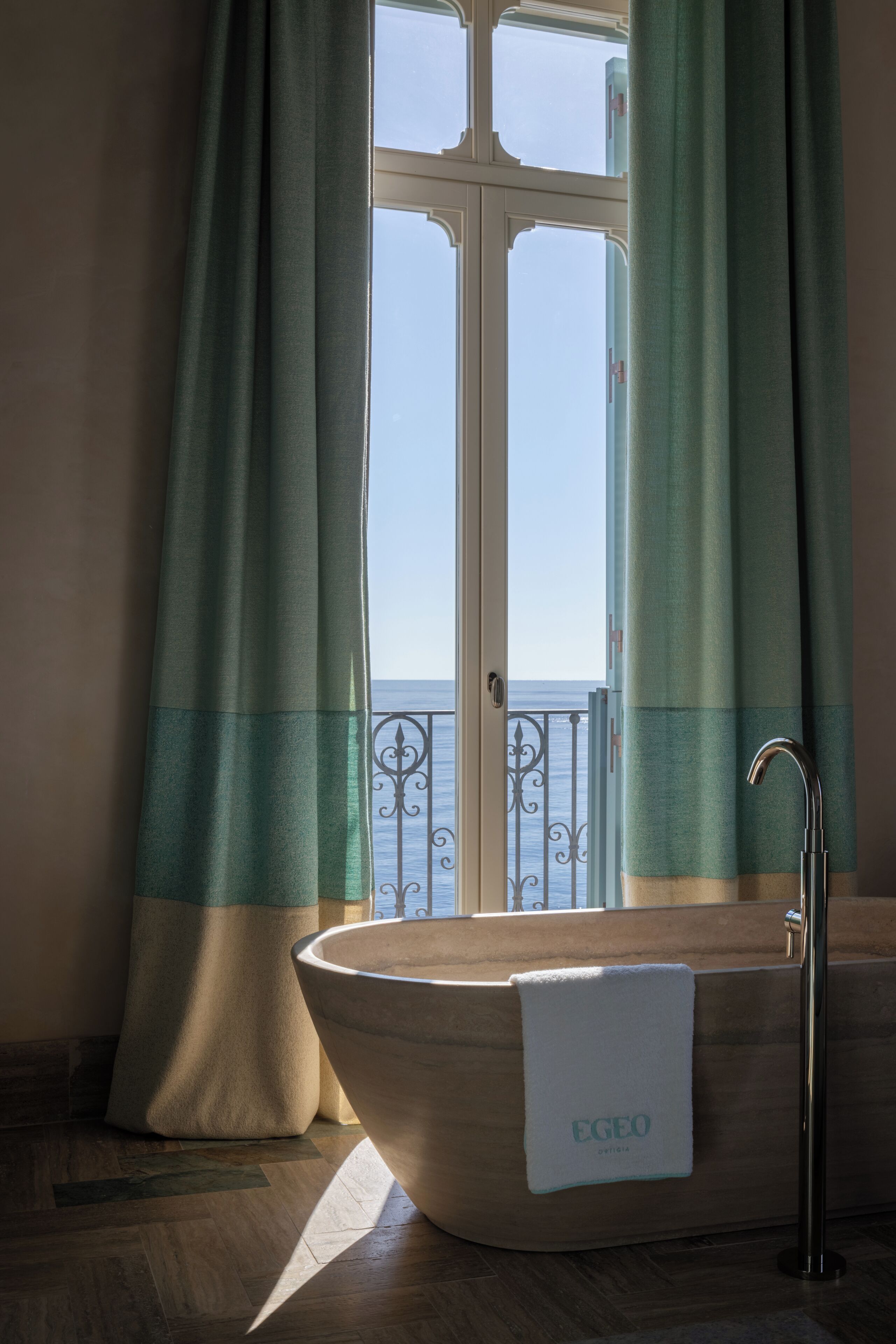 Un baño con bañera independiente, una toalla y vista al mar a través de una ventana.