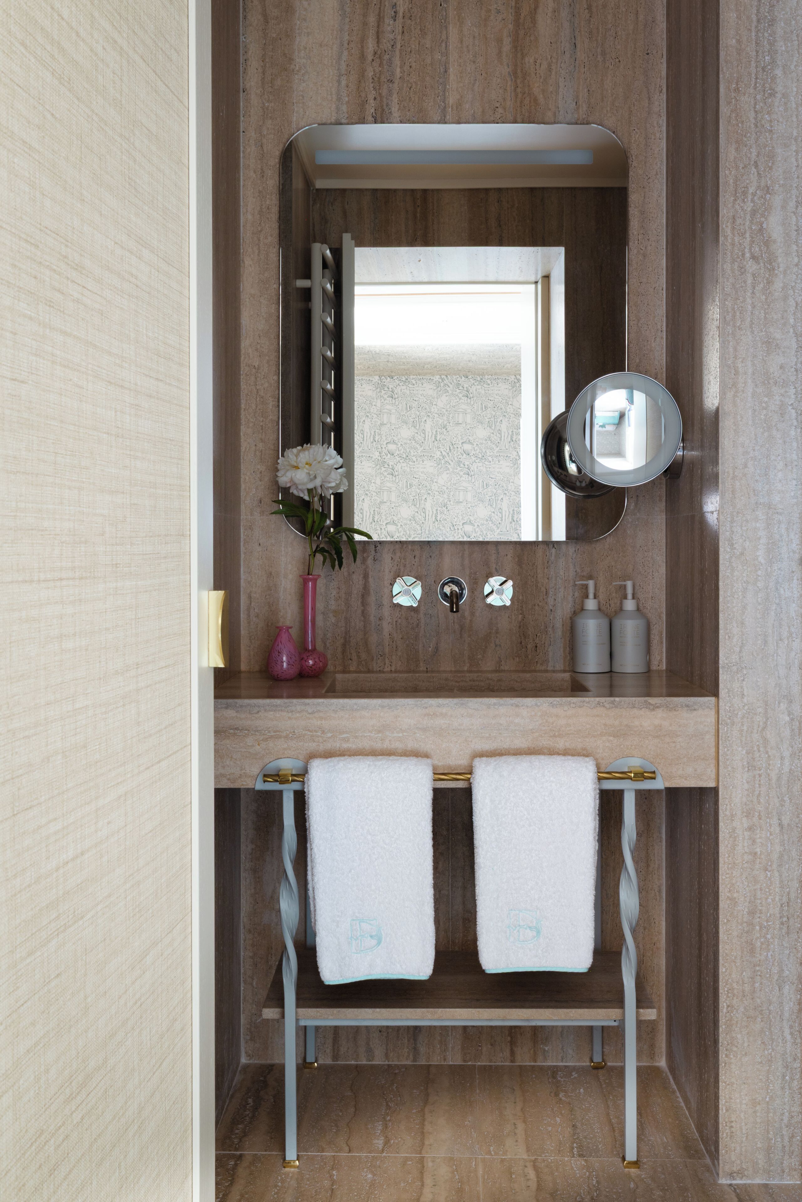 Une salle de bain avec un meuble-lavabo en marbre, un miroir, deux serviettes et un vase avec une fleur.