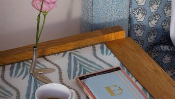 A table with a cup of coffee, a spoon, a book, and a vase with a single pink flower.