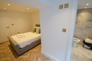 A bedroom with a bed, a bathroom with a toilet, and a herringbone-patterned floor. - Modern Newly Converted  Retreat with Hot Tub - Rye (East Sussex)