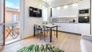 A modern kitchen with white cabinets, a flat-screen TV, and a dining area with a table and chairs. - Hostdomus - Green House (Diano Marina)