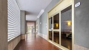 A hallway with a tiled floor, a glass door with a metal grid, and a number '21' sign. - Hostdomus - Green House (Diano Marina)