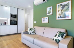 A modern living room with a beige sofa, a green wall, and framed artwork. - Hostdomus - Green House (Diano Marina)