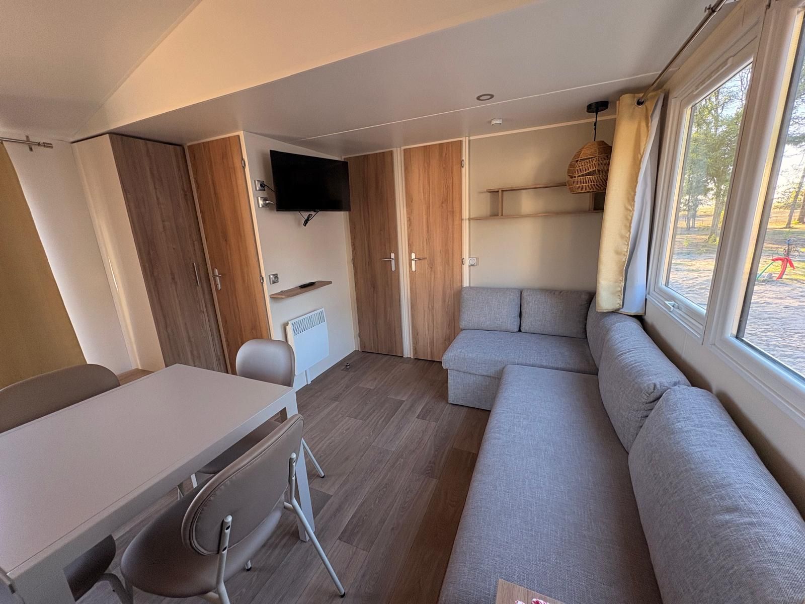 Een knus woongedeelte met een bank, een tafel, een stoel en een aan de muur bevestigde televisie.