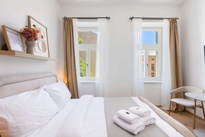 A hotel room with a bed, a chair, a table, a window with curtains, and a shelf with a vase and a framed document. - Central Prague Studio Near Wenceslas Square, (Hlavní město Praha)