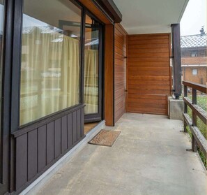 A balcony with a wooden door, a sliding glass door, and a concrete floor. - Chez Katy I Studio I St Jean d'Aulps (Saint-Jean-d'Aulps)