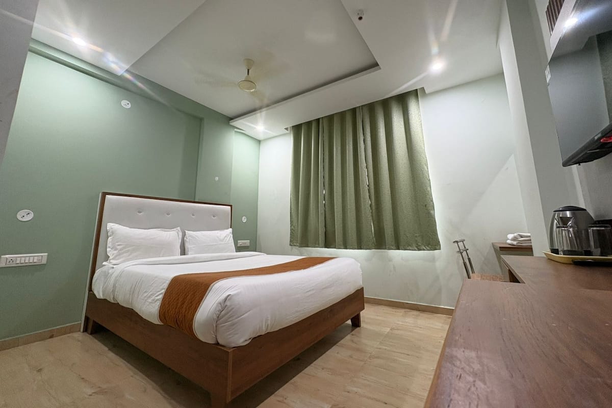 Habitación de hotel con cama, ventilador de techo, ventana con cortinas, cafetera y escritorio de madera.