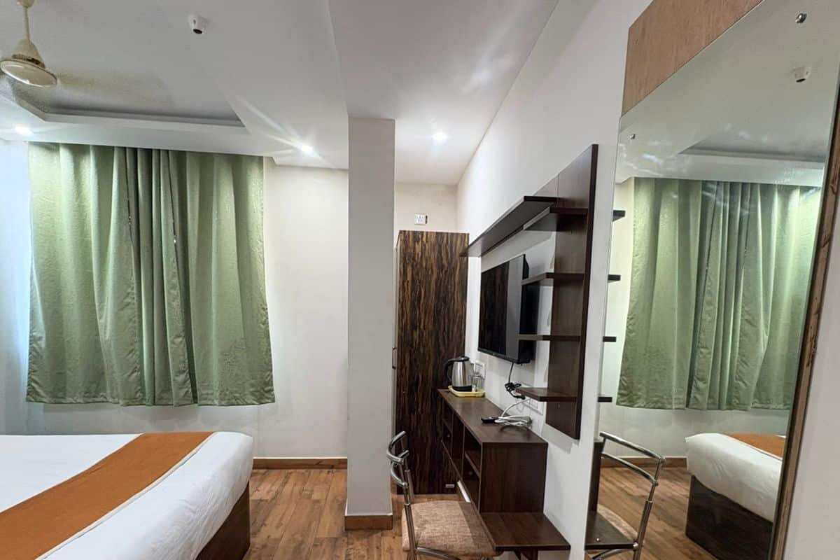 Habitación de hotel con cama, escritorio, silla, televisor, espejo y ventilador de techo.
