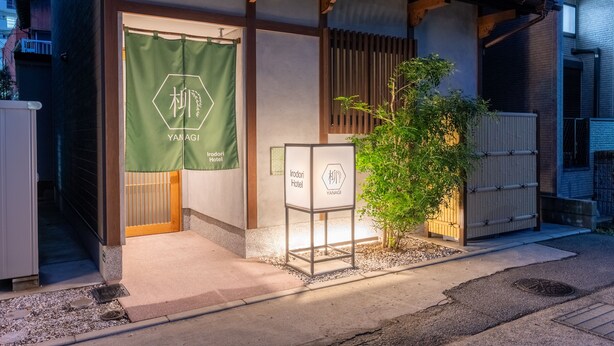 Entrada de hotel con un estandarte verde, un cartel y un pequeño árbol.